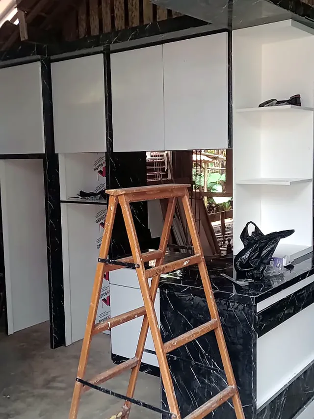 Kitchen set dengan meja motif marmer hitam saat pemasangan, dengan tangga di depannya